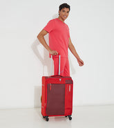 A person standing next to a red American Tourister Marina soft-side luggage bag with four wheels and a telescopic handle.